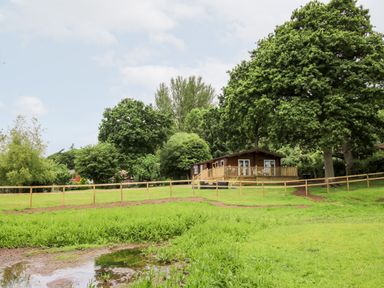 A wooden cabin with a deck surrounded by grass and trees at The Log Cabin in Newnham Bridge near Tenbury Wells