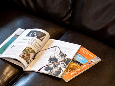 An open magazine and a folded map on a dark leather surface with a pair of glasses