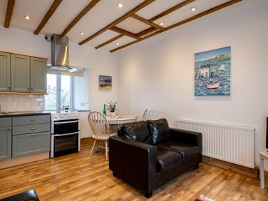 A kitchen and living area with a black sofa a round dining table two chairs and kitchen cabinets at Stable Cottage Port Isaac