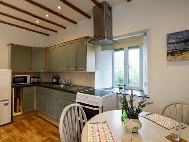A kitchen with green cabinets a stove a refrigerator and a dining table with chairs and placemats at Stable Cottage in Port Isaac