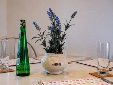 A table with a vase of flowers a green bottle drinking glasses and placemats at Stable Cottage in Port Isaac