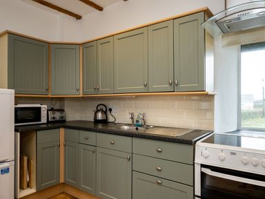 A kitchen with green cabinets a microwave kettle toaster sink and stove at Stable Cottage in Port Isaac