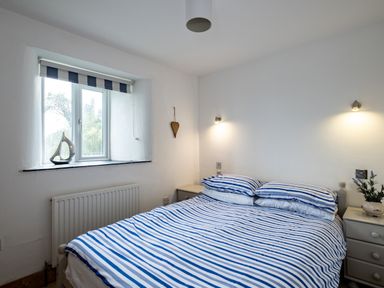 A bedroom with a bed with blue and white striped bedding two bedside tables and a window with a striped blind at Stable Cottage in Port Isaac