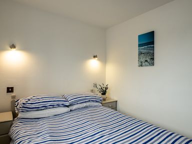 A bedroom with a double bed with blue and white striped bedding two bedside tables with lamps and a wall picture at Stable Cottage in Port Isaac