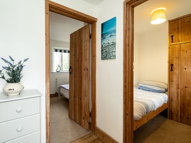 A hallway with two doorways leading to bedrooms and a chest of drawers with a plant on top at Stable Cottage in Port Isaac