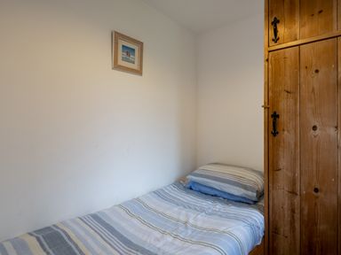 A small bedroom with a single bed with striped bedding a wooden wardrobe and a small picture on the wall at Stable Cottage in Port Isaac