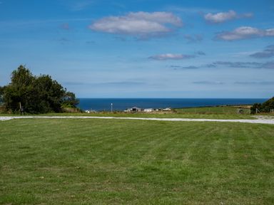 A grassy field with a gravel path and trees near a coastline with buildings and the sea at Stable Cottage in Port Isaac
