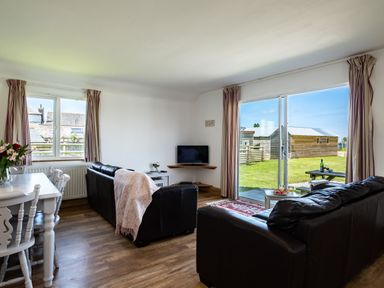 A living room with black leather sofas a small television and dining table with chairs at Atlantic Lodge in Port Isaac