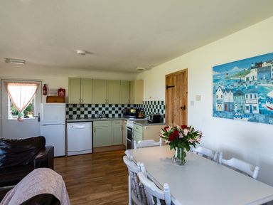 A dining table with flowers and chairs next to a kitchen with cabinets and appliances at Atlantic Lodge in Port Isaac