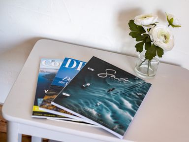 A small table with three magazines and a glass jar with white flowers at Atlantic Lodge in Port Isaac