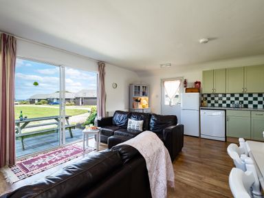 An open plan living room and kitchen with leather sofas table and chairs and sliding glass door at Atlantic Lodge in Port Isaac