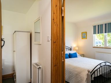 A bedroom with a white bedspread and blue pillows next to a window with striped blinds at Atlantic Lodge in Port Isaac
