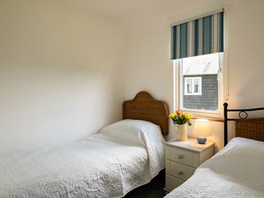 A bedroom with two single beds a nightstand with a lamp and flowers and a window with a striped blind at Atlantic Lodge in Port Isaac
