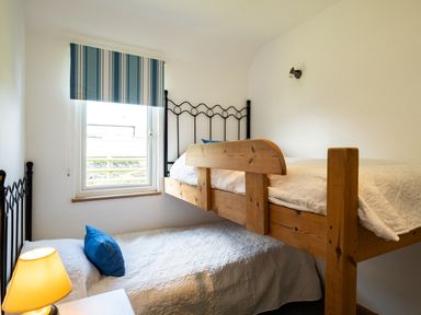 A small bedroom with bunk beds a window with a striped blind and a lamp on a bedside table at Atlantic Lodge in Port Isaac