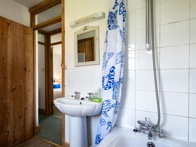 A bathroom with a pedestal sink a mirror a bathtub with a shower and a blue and white shower curtain at Atlantic Lodge in Port Isaac