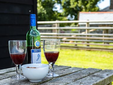 A wooden outdoor table with a bottle of merlot wine two glasses of wine and a white bowl of almonds at Atlantic Lodge in Port Isaac