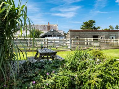 An outdoor garden area with a wooden picnic table and fence near wooden buildings and greenery at Atlantic Lodge in Port Isaac