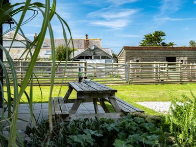 A wooden picnic table with a bottle and glasses on a patio overlooking fenced yard and buildings at Atlantic Lodge in Port Isaac