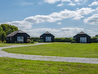 Three small black wooden cabins on a grassy field with a gravel path under a cloudy sky at Atlantic Lodge in Port Isaac