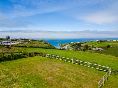 A coastal landscape with green fields a wooden fence and buildings near the sea at Atlantic Lodge in Port Isaac