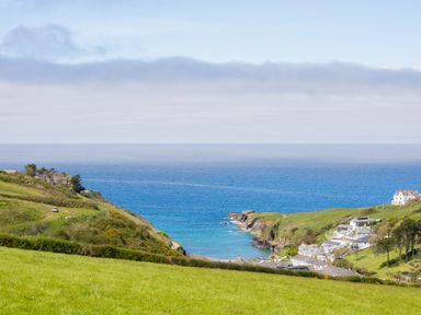 A coastal view with green fields and houses by the sea at Atlantic Lodge in Port Isaac