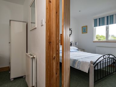 A bedroom with a bed, nightstand, window with striped blinds, wardrobe, and a mirror at Gull Lodge in Port Isaac