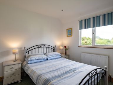A bedroom with a double bed between two bedside tables with lamps and a window with striped blinds at Gull Lodge in Port Isaac
