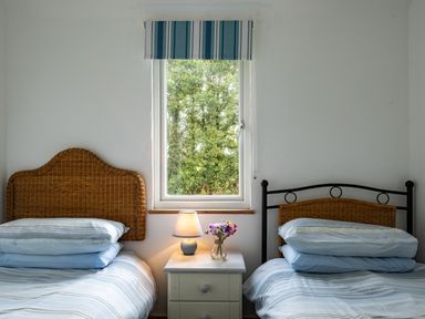 A bedroom with two single beds separated by a bedside table with a lamp and flowers at Gull Lodge in Port Isaac