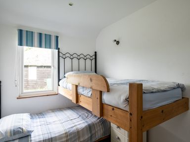 A bedroom with wooden bunk beds and a window with a striped blue blind at Gull Lodge in Port Isaac