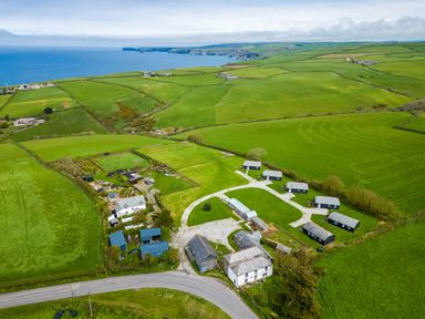 An aerial view of a rural area with houses and green fields near the coast at Gull Lodge in Port Isaac