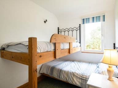A bedroom with wooden bunk beds a window with striped blue blinds and a table lamp at Campion Lodge in Port Isaac