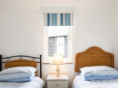 A bedroom with two single beds with wicker headboards a window with a blue striped blind and a lamp on a white bedside table at Campion Lodge in Port Isaac