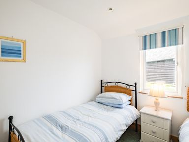 A small bedroom with a single bed a nightstand with a lamp and a window with striped blinds at Campion Lodge in Port Isaac