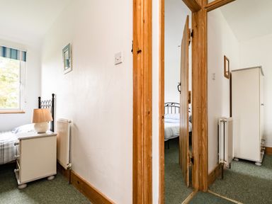 A view of two bedrooms with beds dressers radiators and a wooden door at Campion Lodge in Port Isaac