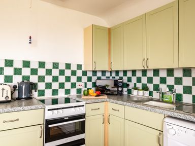 A kitchen with green and white tiled backsplash green cabinets a stove kettle microwave sink and dishwasher at Campion Lodge Port Isaac