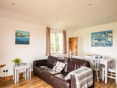 A living room with a brown leather sofa and white dining table with chairs at Campion Lodge in Port Isaac