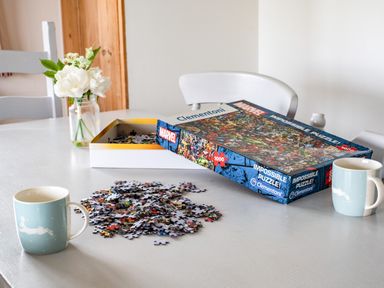 A table with an opened Marvel puzzle box some puzzle pieces two mugs and a jar with white flowers at Campion Lodge in Port Isaac