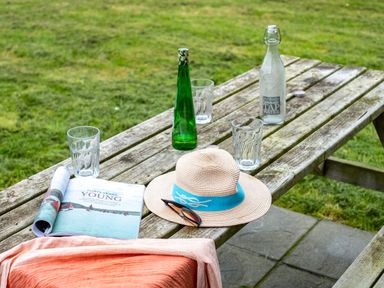 A wooden picnic table outdoors with glasses bottles a magazine a hat and sunglasses at Campion Lodge in Port Isaac