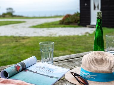 A wooden picnic table with a magazine glass bottle hat and sunglasses outside a building at Campion Lodge in Port Isaac