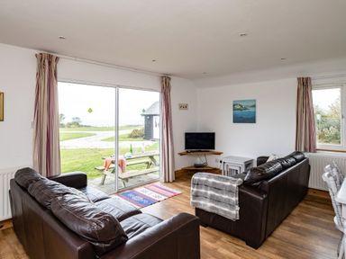 A living room with two dark brown sofas a small television on a corner shelf a window and sliding glass door with curtains at Campion Lodge in Port Isaac