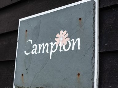 A close up of a weathered stone sign with the word Campion and a flower attached to a dark wooden wall at Campion Lodge in Port Isaac