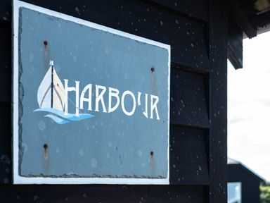 A sign with a sailboat and the word Harbour on a dark wooden wall at Harbour Lodge in Port Isaac