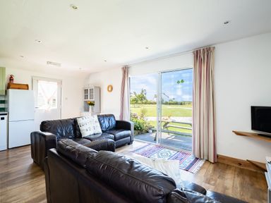 A living room with leather sofas a sliding glass door leading to a garden and a television on a wall at Harbour Lodge in Port Isaac