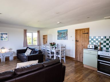 A living room with brown leather sofas a white dining table with chairs a wooden door and a kitchen area at Harbour Lodge in Port Isaac