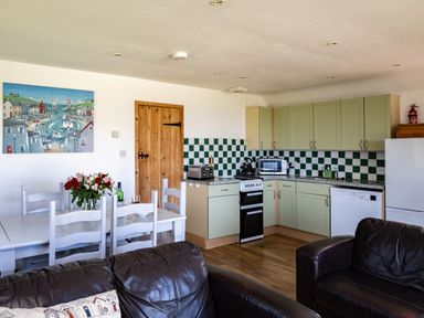 A kitchen and dining area with green cabinets white dining table and leather chairs at Harbour Lodge in Port Isaac