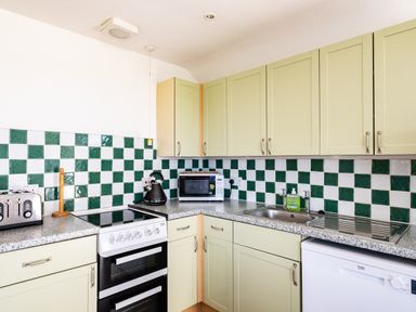 A kitchen with tiled backsplash green and white cabinets stove microwave kettle toaster and sink at Harbour Lodge in Port Isaac