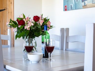 A dining table with two glasses of red drink a green bottle a white bowl and a vase of flowers at Harbour Lodge in Port Isaac