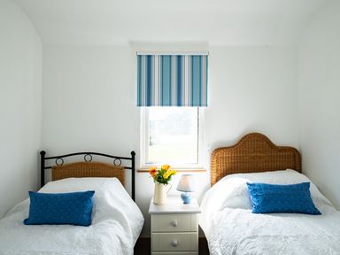 A bedroom with two single beds a dresser in the middle with flowers and a lamp at Harbour Lodge in Port Isaac