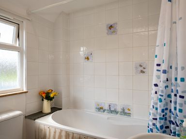 A bathroom with bathtub white tiles with fish designs a window and a vase with flowers at Harbour Lodge in Port Isaac