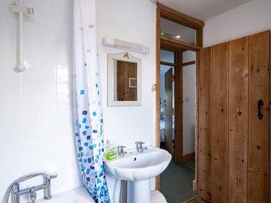 A bathroom with a bathtub shower curtain sink mirror and wooden door at Harbour Lodge Port Isaac